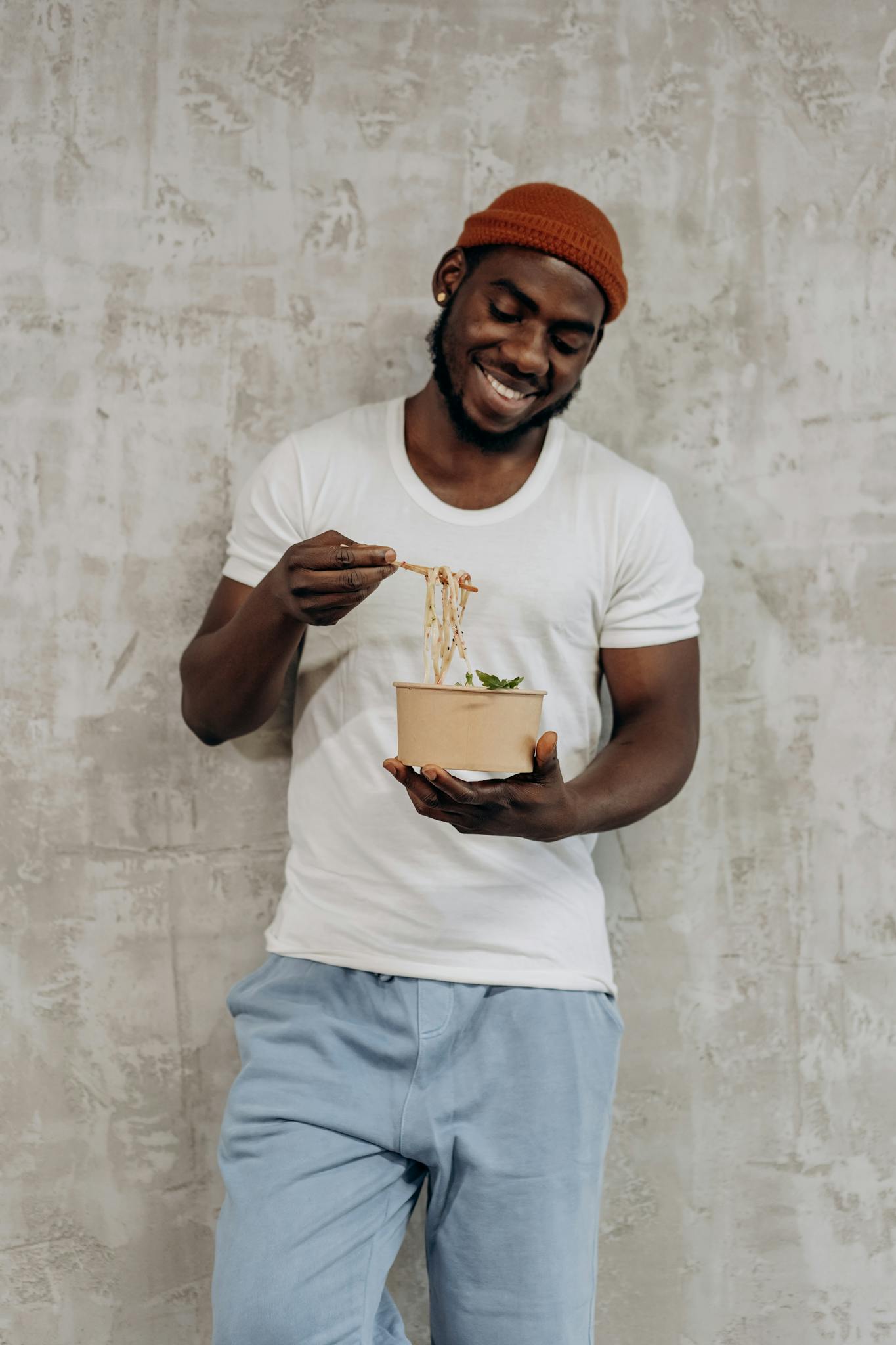 Man in casual outfit smiling while eating noodles from a bowl. Perfect for lifestyle and healthy eating concepts.